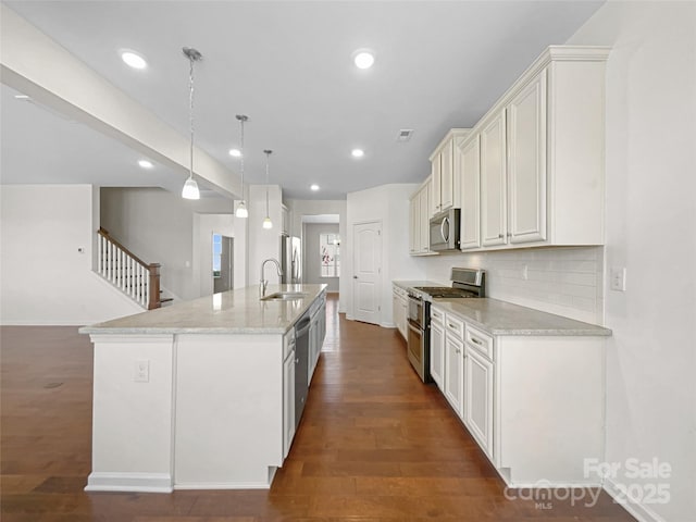 kitchen featuring pendant lighting, sink, light stone counters, a kitchen island with sink, and stainless steel appliances