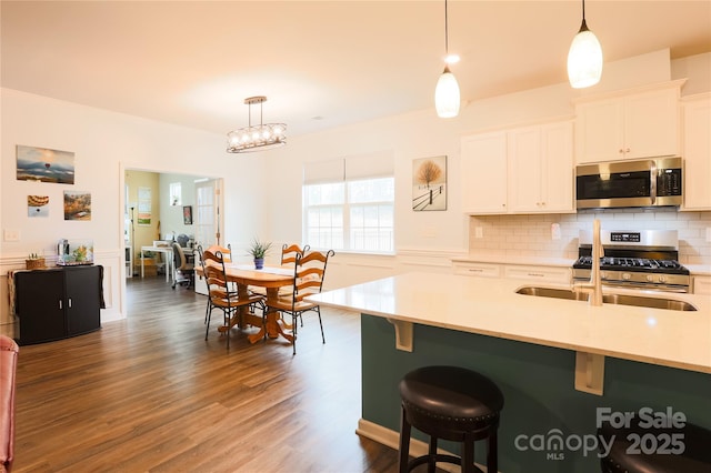 kitchen with hanging light fixtures, appliances with stainless steel finishes, backsplash, white cabinets, and a breakfast bar area