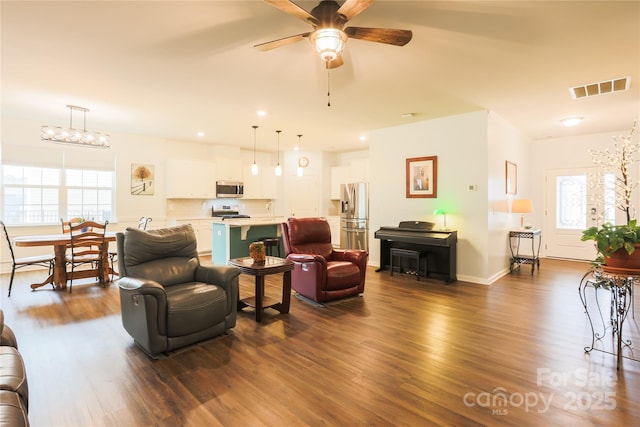 living room with ceiling fan with notable chandelier, dark hardwood / wood-style floors, and plenty of natural light