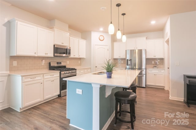 kitchen featuring a kitchen bar, appliances with stainless steel finishes, white cabinetry, decorative light fixtures, and a center island with sink