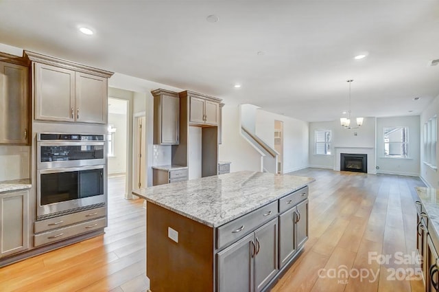 kitchen featuring light stone countertops, decorative backsplash, light wood-type flooring, a kitchen island, and double oven