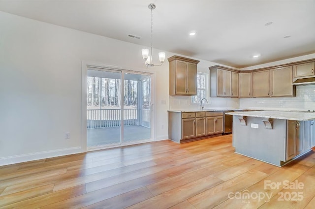 kitchen with a center island, hanging light fixtures, stainless steel dishwasher, light hardwood / wood-style flooring, and a breakfast bar area