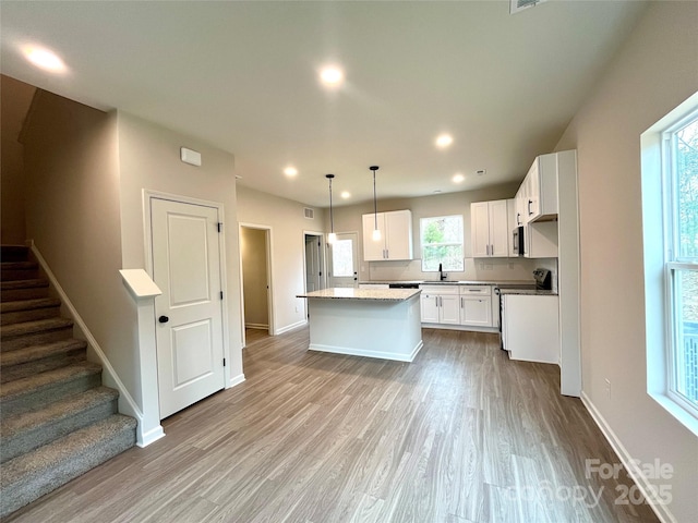 kitchen with light hardwood / wood-style floors, stove, a kitchen island, pendant lighting, and white cabinets