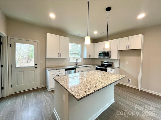 kitchen featuring pendant lighting, a kitchen island, white cabinetry, light stone countertops, and stainless steel appliances