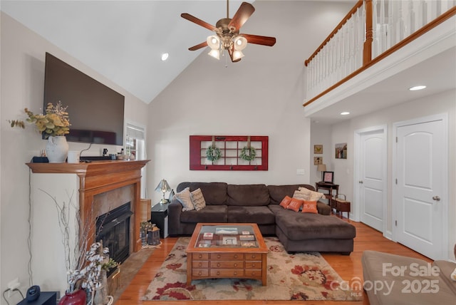 living room featuring ceiling fan, a fireplace, light hardwood / wood-style flooring, and high vaulted ceiling