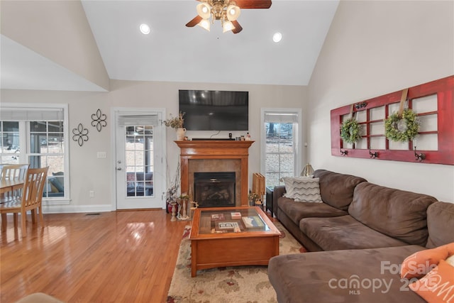 living room featuring light wood-type flooring, ceiling fan, a fireplace, and high vaulted ceiling