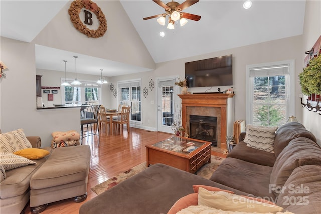 living room featuring high vaulted ceiling, hardwood / wood-style flooring, a tile fireplace, and a healthy amount of sunlight