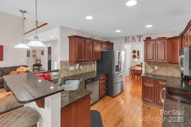 kitchen with kitchen peninsula, appliances with stainless steel finishes, decorative light fixtures, dark stone countertops, and sink