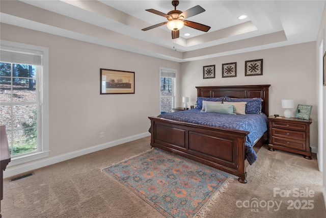 bedroom featuring ceiling fan, a tray ceiling, and light carpet