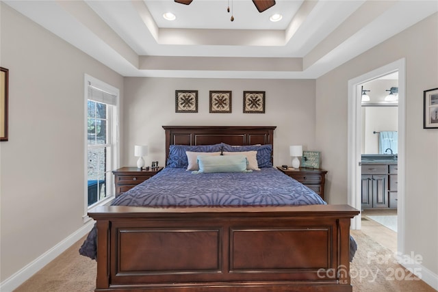 carpeted bedroom featuring ceiling fan, a tray ceiling, and ensuite bath