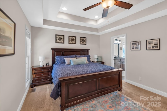 bedroom with ensuite bathroom, light colored carpet, ceiling fan, and a raised ceiling