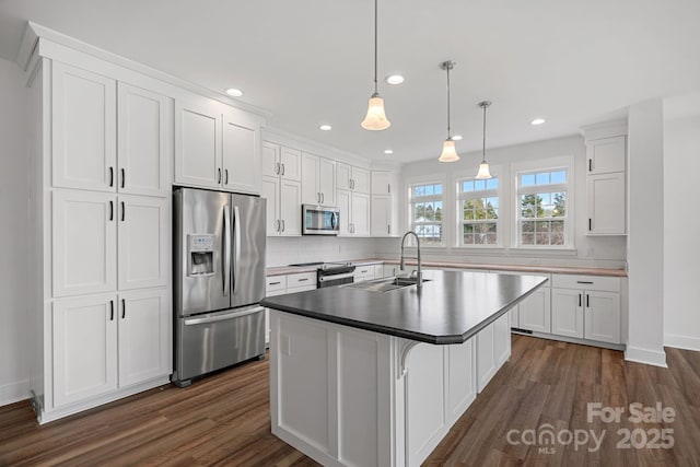 kitchen featuring pendant lighting, sink, appliances with stainless steel finishes, white cabinetry, and an island with sink