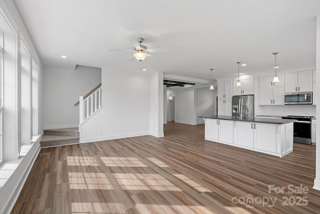 kitchen with white cabinetry, hanging light fixtures, an island with sink, stainless steel appliances, and backsplash