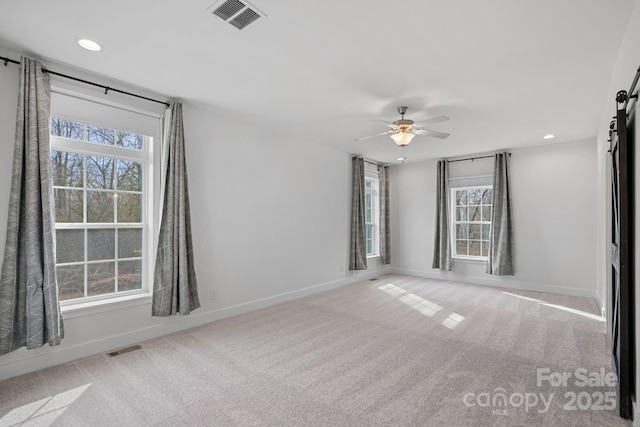 spare room featuring a barn door, a healthy amount of sunlight, light carpet, and ceiling fan