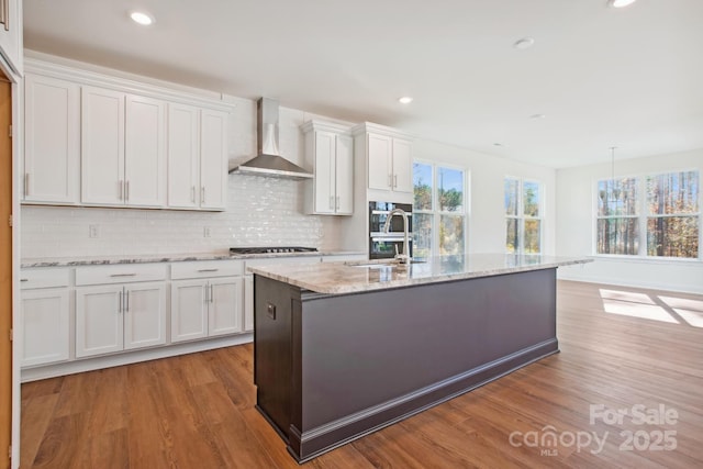 kitchen featuring light hardwood / wood-style flooring, wall chimney exhaust hood, sink, white cabinetry, and a center island with sink