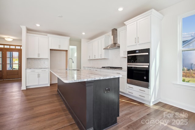 kitchen with wall chimney exhaust hood, a kitchen island with sink, and white cabinetry