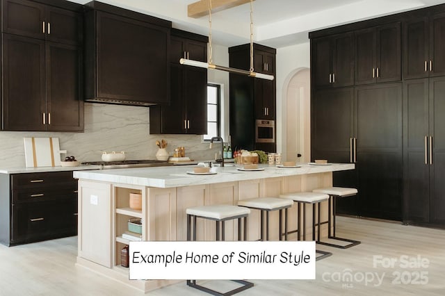 kitchen featuring a center island with sink, appliances with stainless steel finishes, a kitchen bar, and tasteful backsplash