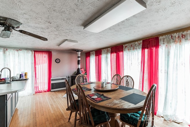 dining room with light hardwood / wood-style floors, a textured ceiling, heating unit, and ceiling fan