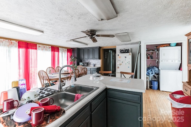 kitchen with ceiling fan, light hardwood / wood-style flooring, a textured ceiling, and stacked washer and dryer