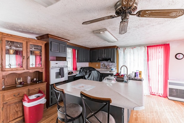 kitchen featuring a textured ceiling, double oven, an island with sink, sink, and light hardwood / wood-style flooring