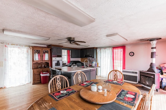 dining area featuring a wood stove, ceiling fan, light hardwood / wood-style floors, and a textured ceiling