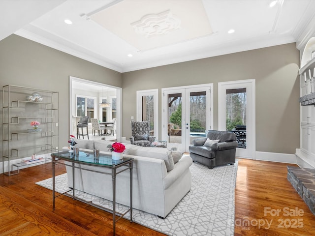 living room featuring hardwood / wood-style floors, ornamental molding, a raised ceiling, and french doors