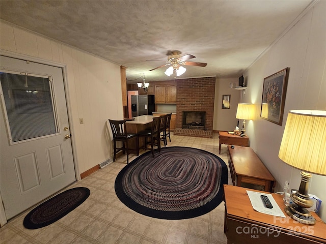 living room with a brick fireplace, crown molding, wooden walls, a textured ceiling, and ceiling fan with notable chandelier