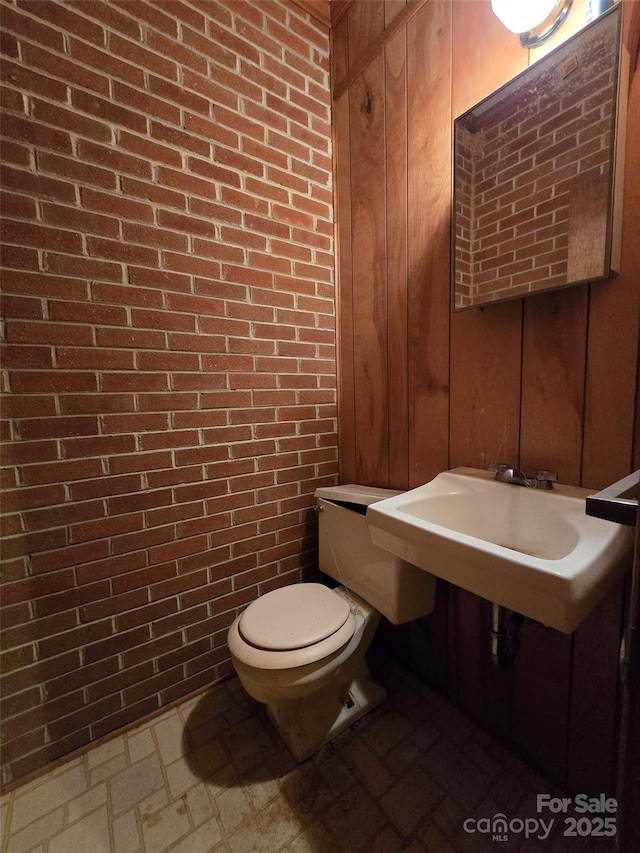 bathroom featuring brick wall, toilet, and wood walls