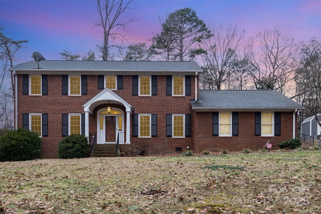 colonial home featuring crawl space, brick siding, a front lawn, and roof with shingles