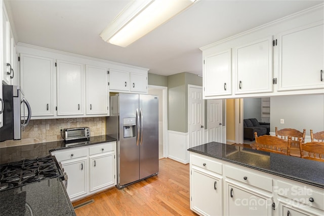 kitchen featuring white cabinets, appliances with stainless steel finishes, decorative backsplash, dark stone counters, and light wood finished floors