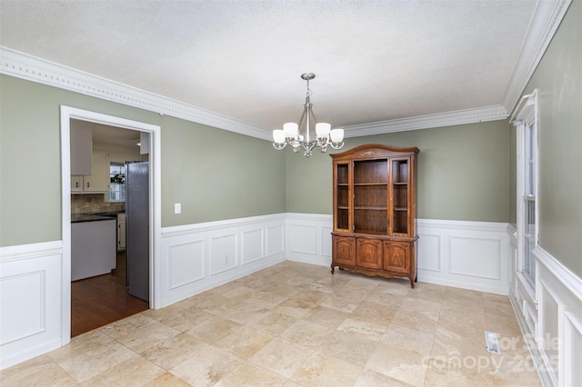 empty room featuring a chandelier, crown molding, a decorative wall, and a textured ceiling