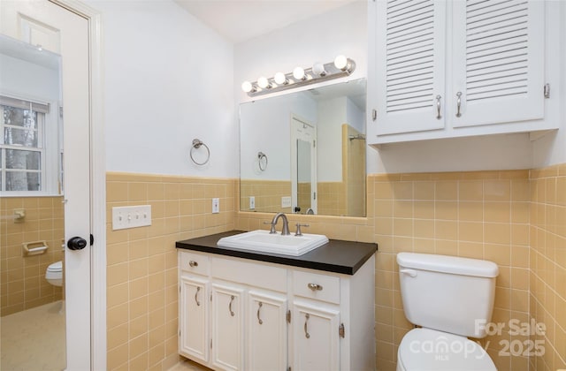 bathroom featuring toilet, wainscoting, tile walls, and vanity