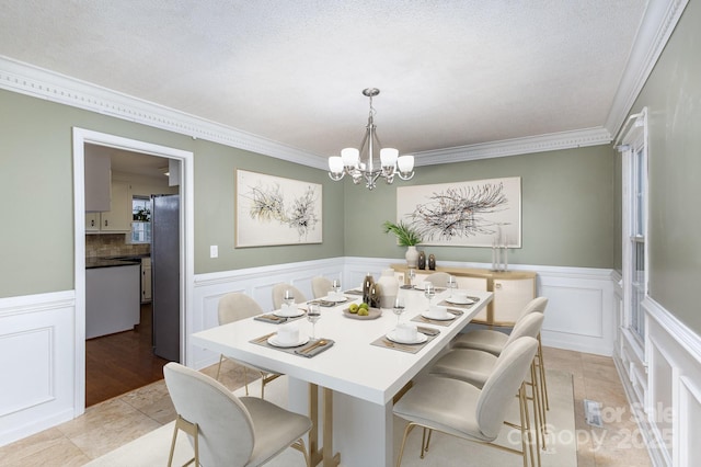 dining space with ornamental molding, a wainscoted wall, a textured ceiling, and an inviting chandelier