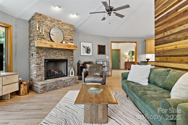 living room with ceiling fan, vaulted ceiling, wood walls, light hardwood / wood-style flooring, and a stone fireplace