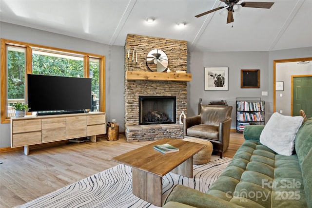 living room with ceiling fan, lofted ceiling, a stone fireplace, and light hardwood / wood-style floors