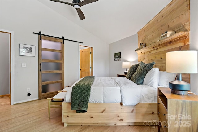 bedroom with vaulted ceiling, ceiling fan, a barn door, and hardwood / wood-style flooring