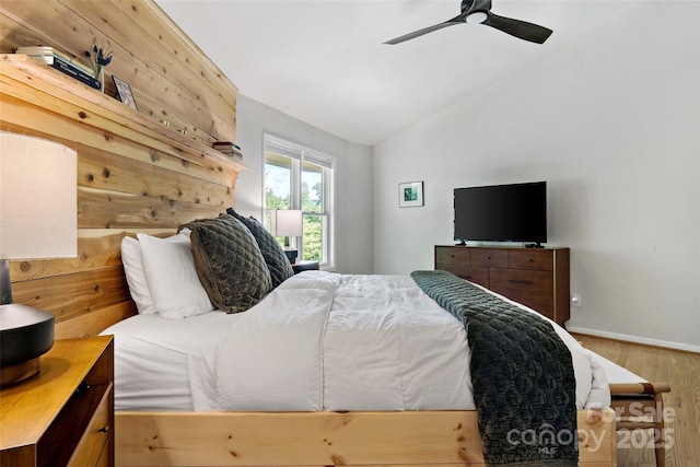 bedroom featuring ceiling fan, hardwood / wood-style floors, wooden walls, and vaulted ceiling