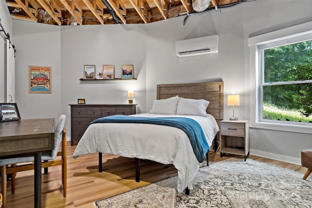 bedroom featuring a wall mounted AC, a barn door, and hardwood / wood-style floors