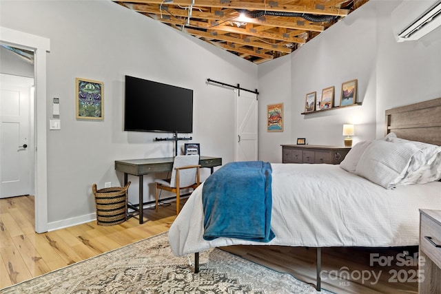 bedroom with a barn door, wood-type flooring, and a wall unit AC