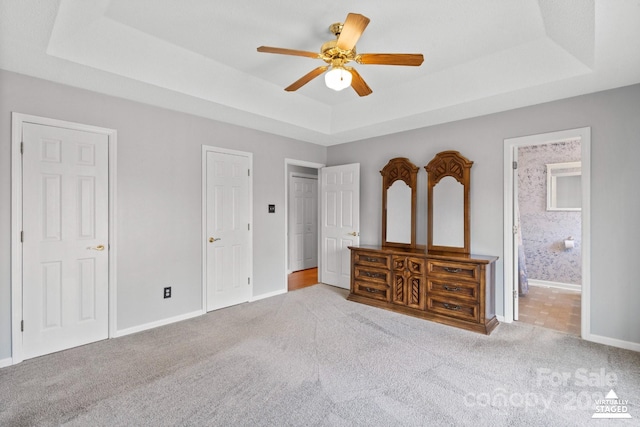 bedroom featuring light colored carpet, a raised ceiling, ceiling fan, and ensuite bathroom