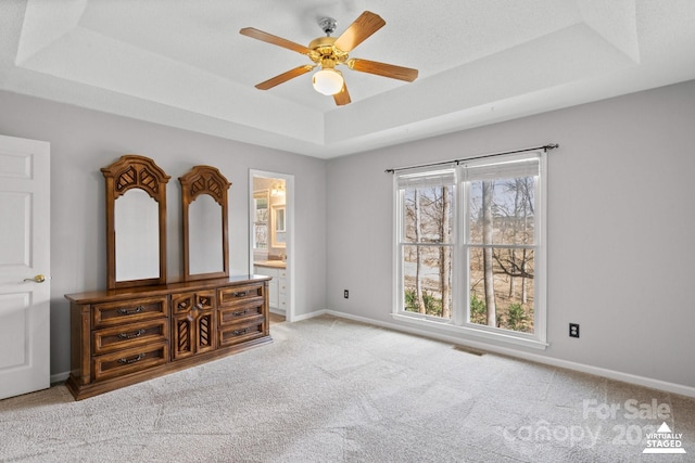 unfurnished bedroom featuring light carpet, a tray ceiling, ensuite bath, and ceiling fan