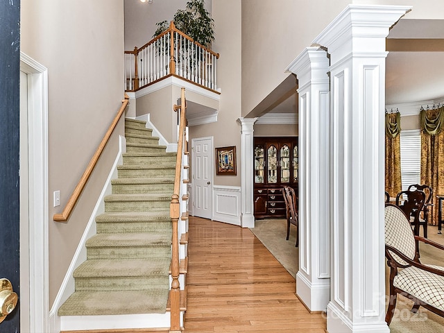 stairway featuring hardwood / wood-style flooring, ornamental molding, and decorative columns