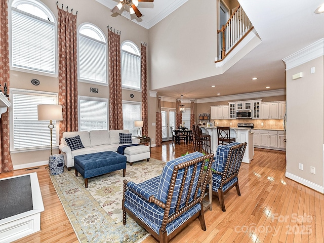 living room featuring ornamental molding, a towering ceiling, ceiling fan, and light wood-type flooring