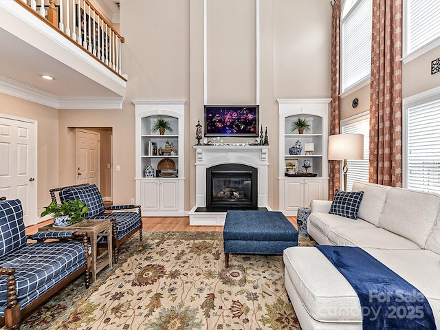 living room with hardwood / wood-style floors, crown molding, built in features, and a high ceiling