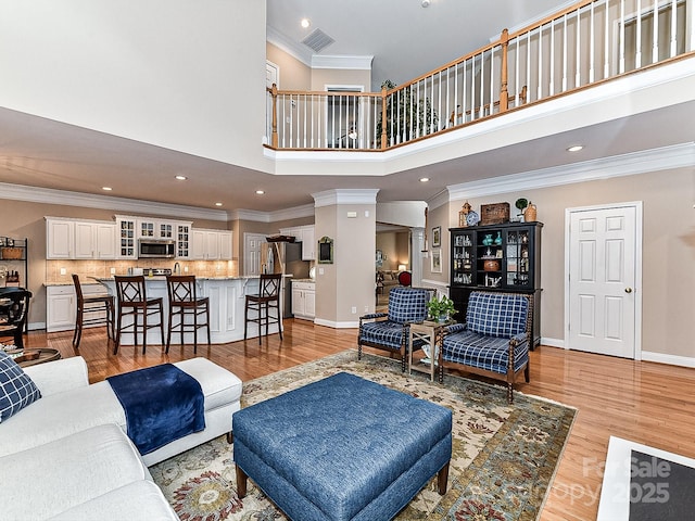 living room with ornate columns, crown molding, a towering ceiling, and light wood-type flooring