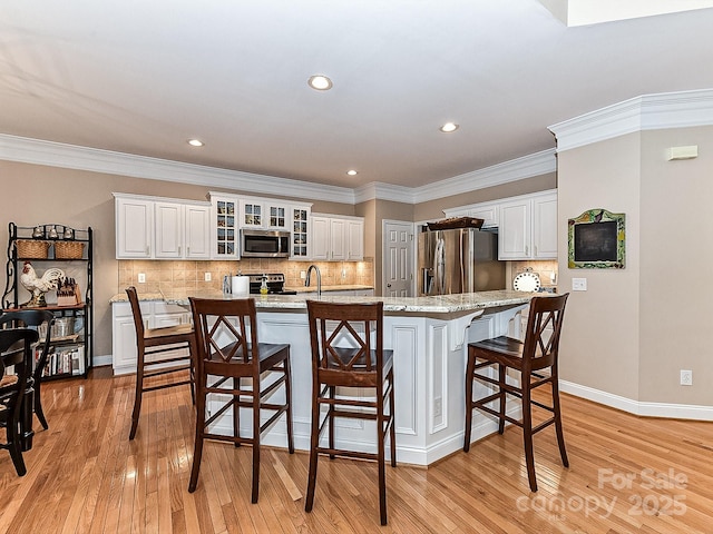 kitchen featuring a breakfast bar, appliances with stainless steel finishes, white cabinetry, light stone counters, and ornamental molding