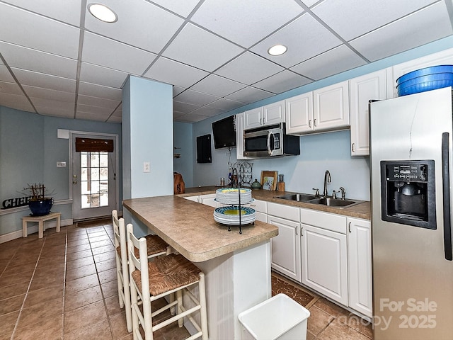 kitchen with a kitchen bar, sink, white cabinetry, a paneled ceiling, and stainless steel appliances