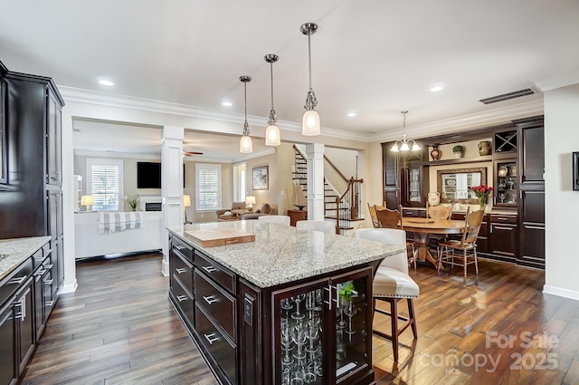 kitchen with dark brown cabinets, hanging light fixtures, a center island, decorative columns, and a breakfast bar area