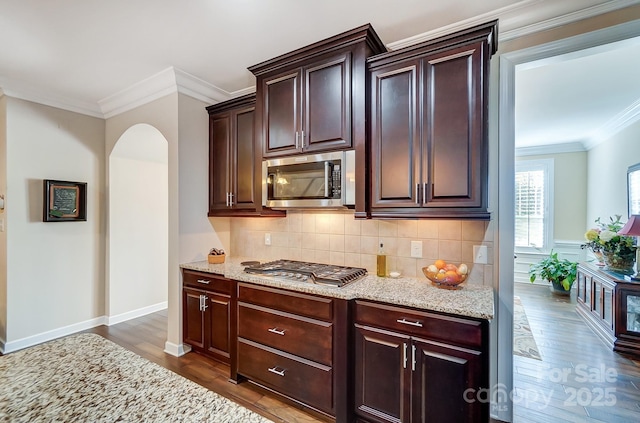 kitchen with crown molding, dark hardwood / wood-style flooring, backsplash, light stone countertops, and stainless steel appliances