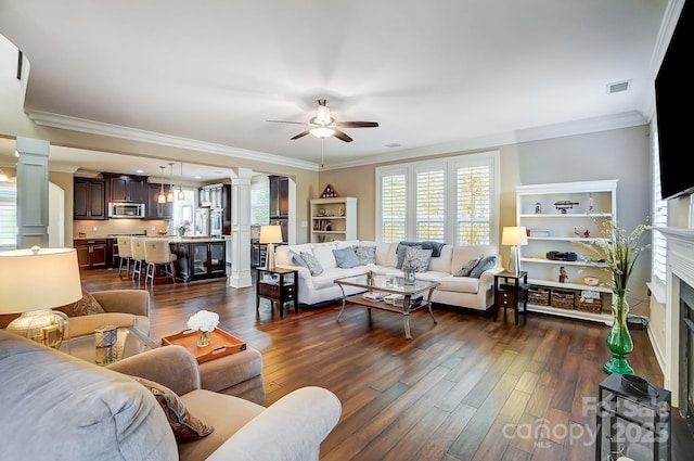 living room with decorative columns, dark wood-type flooring, ceiling fan, and ornamental molding